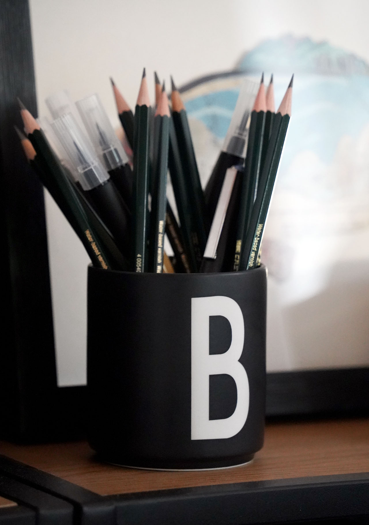 Das Bild zeigt eine schwarze Tasse mit einem weißen B darauf. Die Tasse ist gefüllt mit Bleistiften und Kalligrafie-Markern von Baier Creative in Bayreuth.